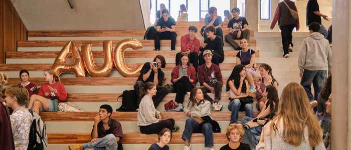 Group of AUC students on the stairs of the AUC building with A, U, C gold balloons